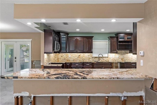 kitchen featuring stainless steel microwave, a sink, tasteful backsplash, dark brown cabinetry, and french doors