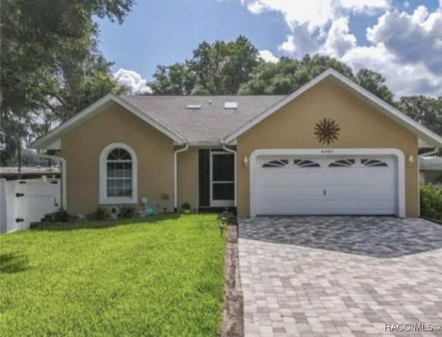 ranch-style home with stucco siding, decorative driveway, an attached garage, and a front lawn