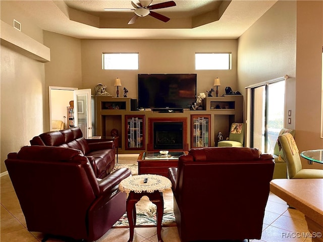 tiled living room featuring a high ceiling, a tray ceiling, and ceiling fan