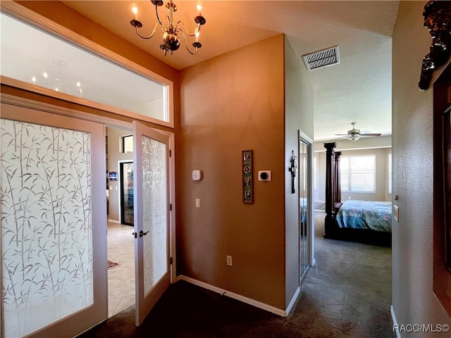 entryway with french doors, ceiling fan with notable chandelier, and dark colored carpet