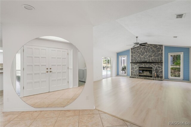 tiled entrance foyer featuring ceiling fan, a stone fireplace, washer / dryer, vaulted ceiling, and visible vents