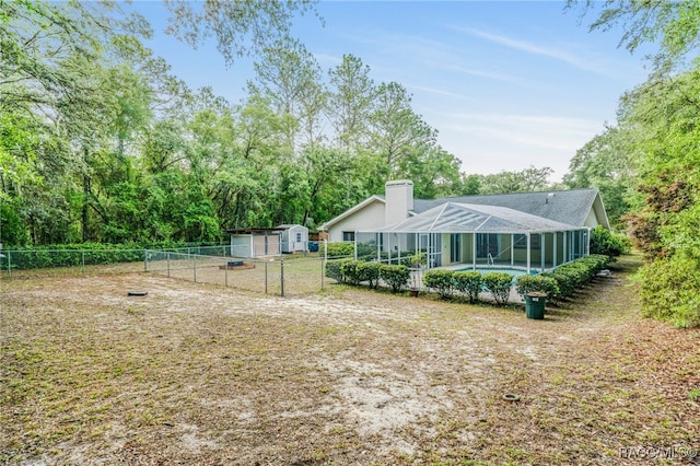 back of house featuring a lanai, a chimney, a fenced in pool, a fenced backyard, and a shed
