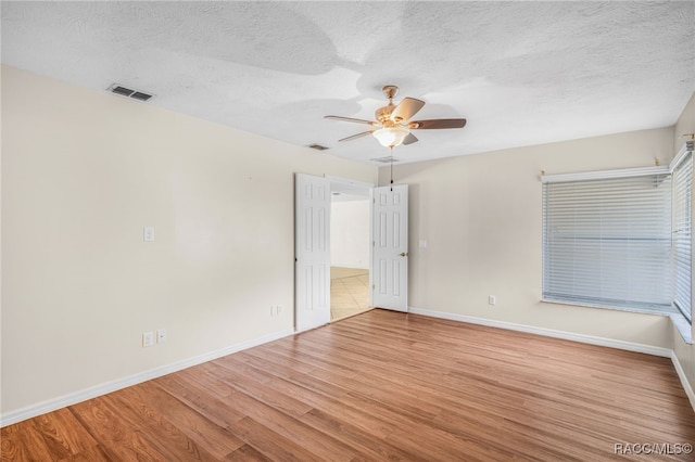 unfurnished room with a ceiling fan, a textured ceiling, visible vents, wood finished floors, and baseboards