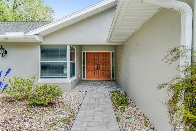 property entrance with a shingled roof and stucco siding