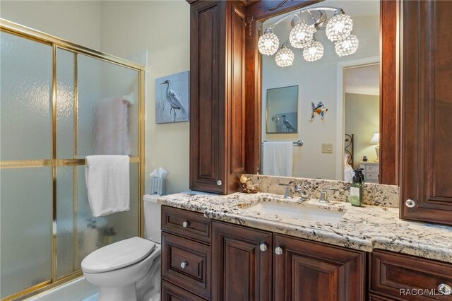 bathroom featuring toilet, vanity, an inviting chandelier, and a shower with door