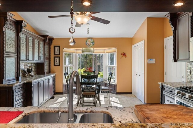 kitchen with lofted ceiling, sink, ceiling fan, dark brown cabinets, and light stone counters