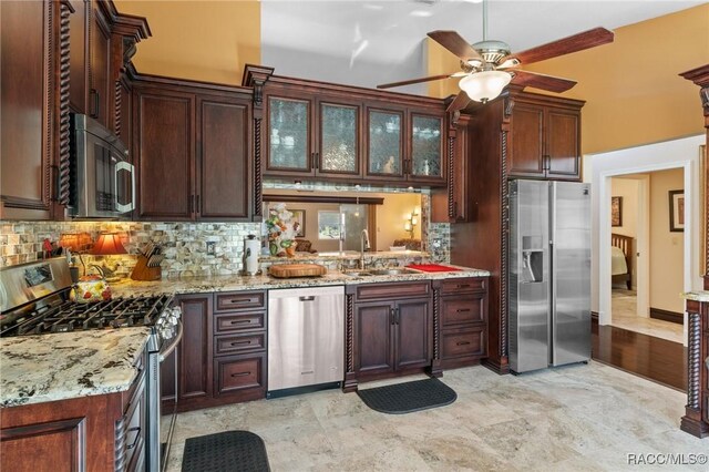 kitchen featuring light stone countertops, ceiling fan, sink, stainless steel appliances, and decorative backsplash