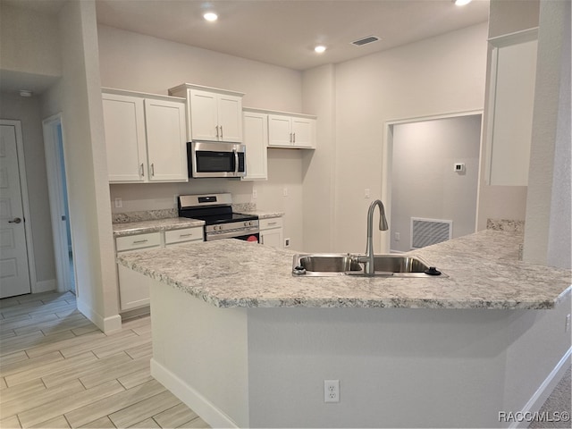 kitchen with kitchen peninsula, light stone countertops, stainless steel appliances, sink, and white cabinets