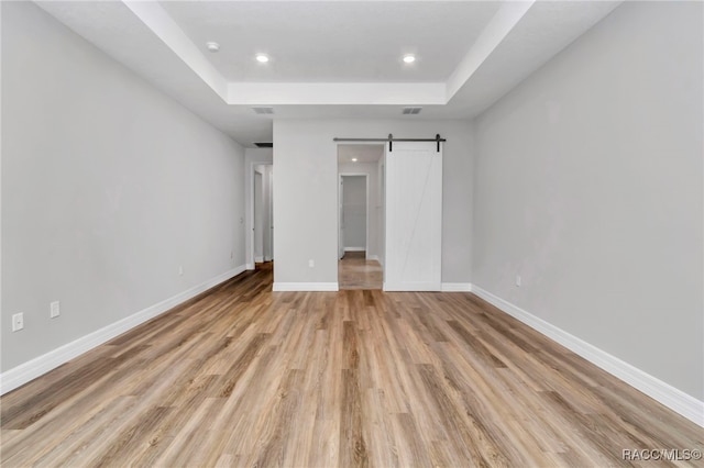 7024 N Fountainhead Dr, Citrus Springs, FL 34433 - unfurnished bedroom featuring a tray ceiling, light wood-style flooring, a barn door, recessed lighting, and a spacious closet