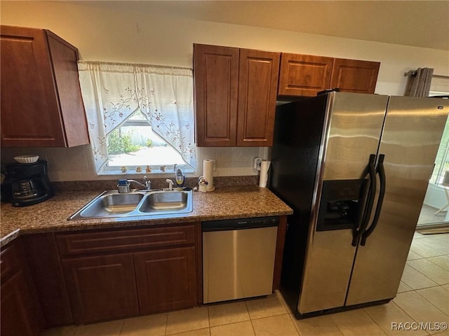 kitchen with a sink, dark countertops, light tile patterned flooring, and stainless steel appliances