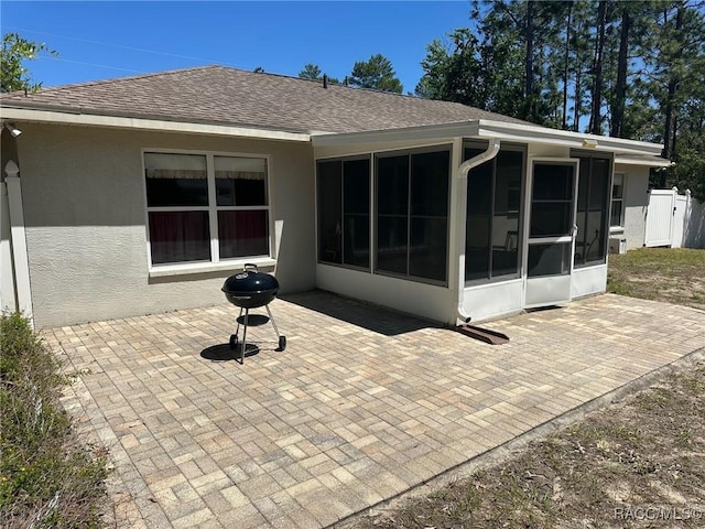 back of property with a patio, stucco siding, a sunroom, and a shingled roof