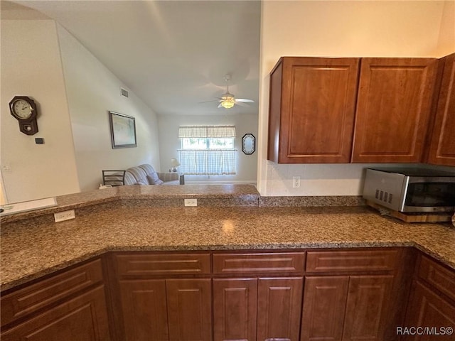 kitchen featuring dark stone counters, a ceiling fan, visible vents, stainless steel microwave, and open floor plan