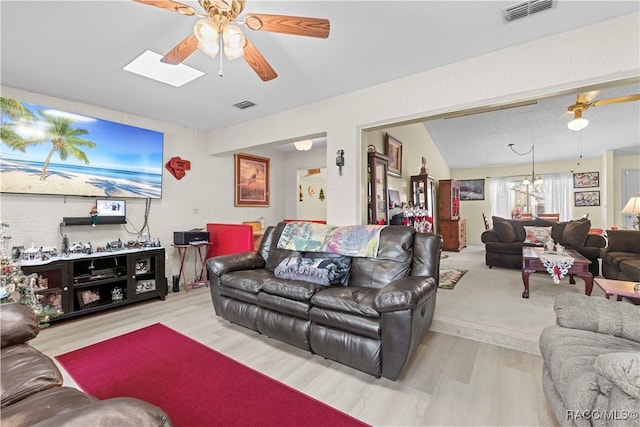 living room with a skylight, ceiling fan with notable chandelier, and light hardwood / wood-style flooring