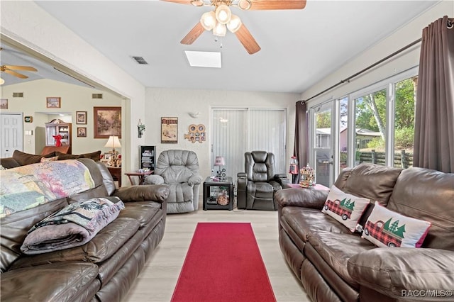 living room featuring ceiling fan, a skylight, and light hardwood / wood-style floors