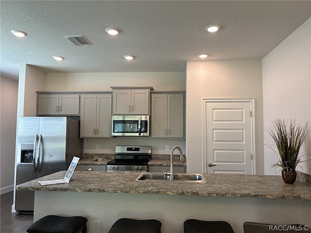 kitchen featuring a kitchen breakfast bar, gray cabinets, sink, and appliances with stainless steel finishes