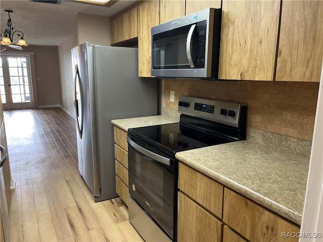 kitchen featuring appliances with stainless steel finishes, backsplash, light hardwood / wood-style flooring, a notable chandelier, and hanging light fixtures