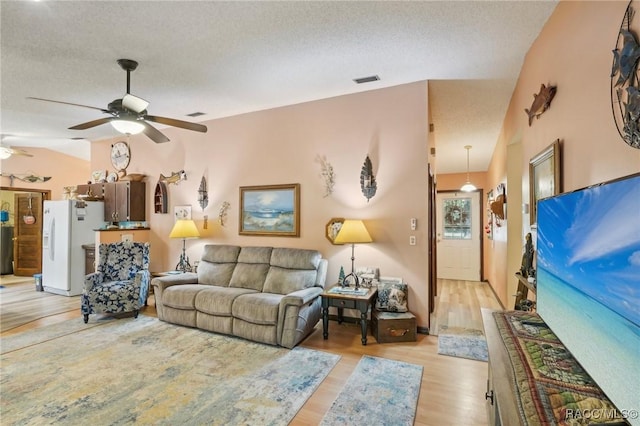 living area with light wood-style floors, a ceiling fan, a textured ceiling, and vaulted ceiling