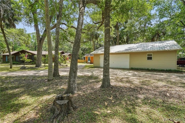 exterior space with an outdoor structure, an attached garage, metal roof, and dirt driveway