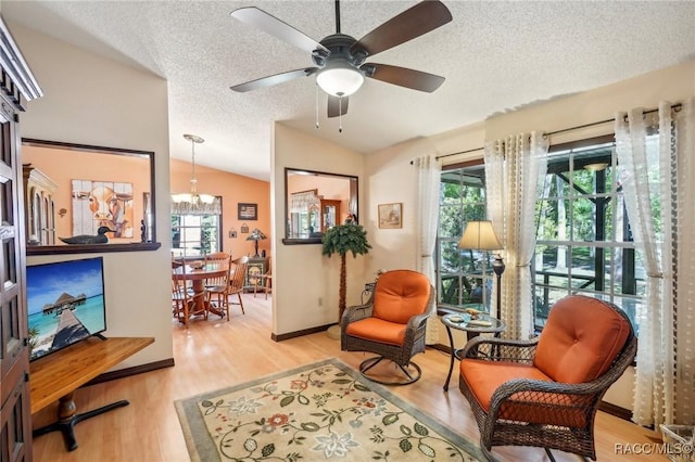living area featuring ceiling fan with notable chandelier, vaulted ceiling, a textured ceiling, and a wealth of natural light