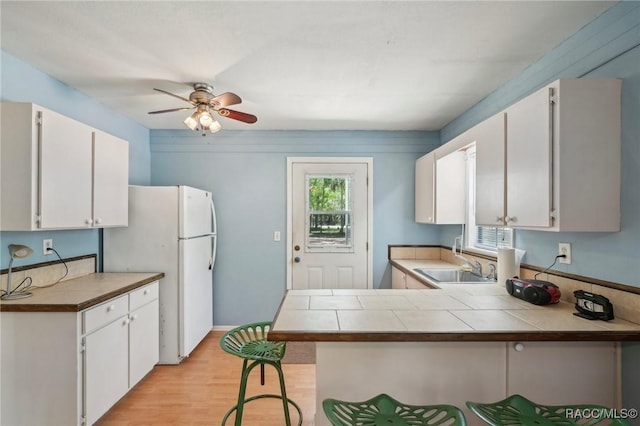 kitchen with a sink, white cabinets, freestanding refrigerator, a peninsula, and light wood-style flooring