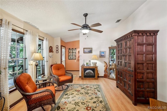 sitting room with a ceiling fan, a textured ceiling, visible vents, vaulted ceiling, and light wood-type flooring
