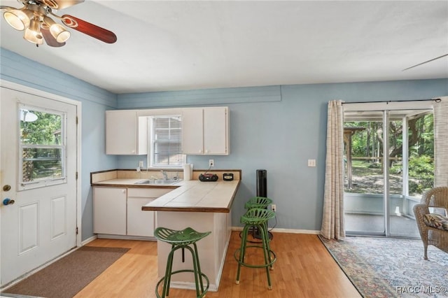 kitchen with tile counters, a sink, light wood-style floors, and white cabinets