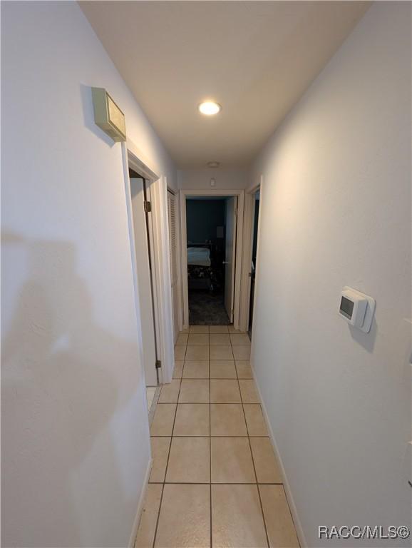 hallway featuring baseboards, light tile patterned floors, and recessed lighting