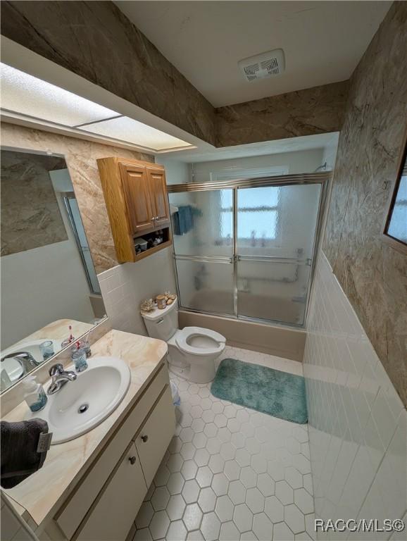 bathroom featuring combined bath / shower with glass door, tile walls, vanity, tile patterned floors, and toilet