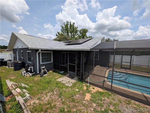 rear view of property with a shingled roof, roof mounted solar panels, and glass enclosure