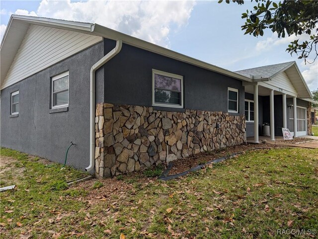 back of house featuring stucco siding, stone siding, a lawn, and a sunroom