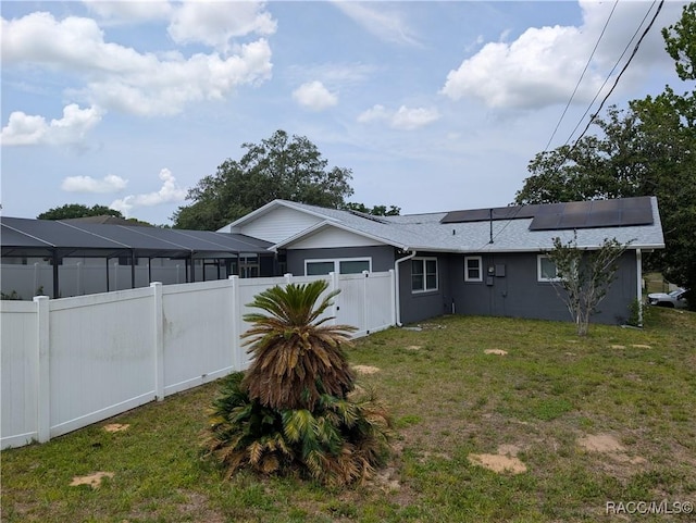 back of house with roof mounted solar panels and roof with shingles