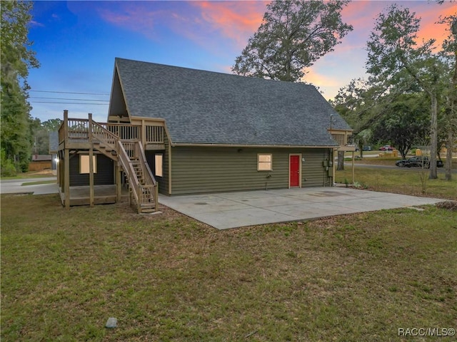 back house at dusk featuring a lawn, a patio area, and a deck