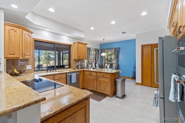 kitchen with appliances with stainless steel finishes, pendant lighting, tasteful backsplash, sink, and kitchen peninsula