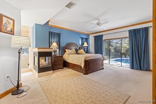 carpeted bedroom with a multi sided fireplace, ensuite bathroom, ornamental molding, access to outside, and ceiling fan