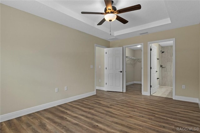977 W Homeway Loop, Citrus Springs, FL 34434 - unfurnished bedroom featuring wood finished floors, a spacious closet, a tray ceiling, ensuite bath, and a ceiling fan