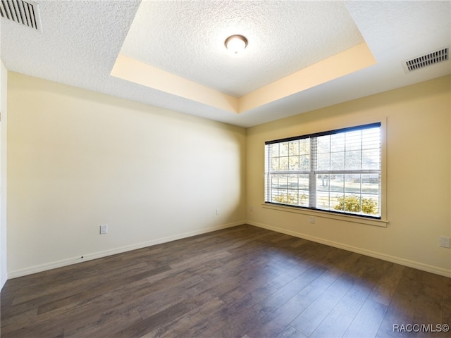 empty room featuring a tray ceiling, a textured ceiling, and dark hardwood / wood-style floors