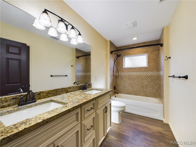 full bathroom with vanity, a textured ceiling, tiled shower / bath combo, hardwood / wood-style flooring, and toilet