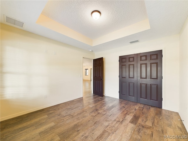 unfurnished bedroom with a textured ceiling, dark hardwood / wood-style floors, a raised ceiling, and a closet