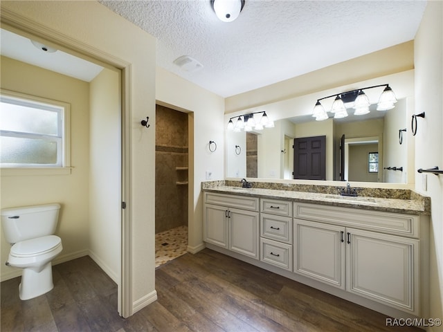 bathroom featuring a tile shower, vanity, a textured ceiling, hardwood / wood-style floors, and toilet