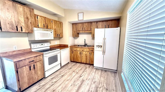 kitchen featuring a sink, brown cabinetry, light wood-style flooring, vaulted ceiling, and white appliances