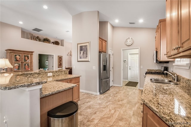 kitchen with stainless steel fridge with ice dispenser, light stone countertops, sink, and kitchen peninsula