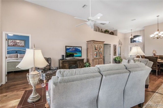 living room featuring wood-type flooring, ceiling fan with notable chandelier, and a high ceiling