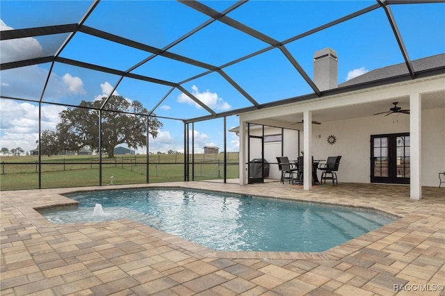 view of swimming pool featuring french doors, pool water feature, ceiling fan, glass enclosure, and a patio area