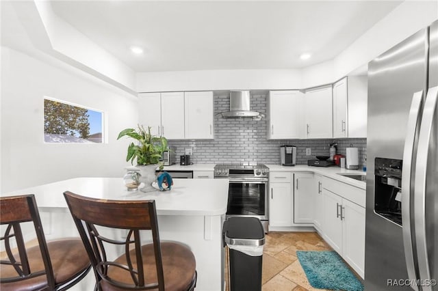 kitchen with stainless steel appliances, white cabinetry, a breakfast bar, and wall chimney exhaust hood