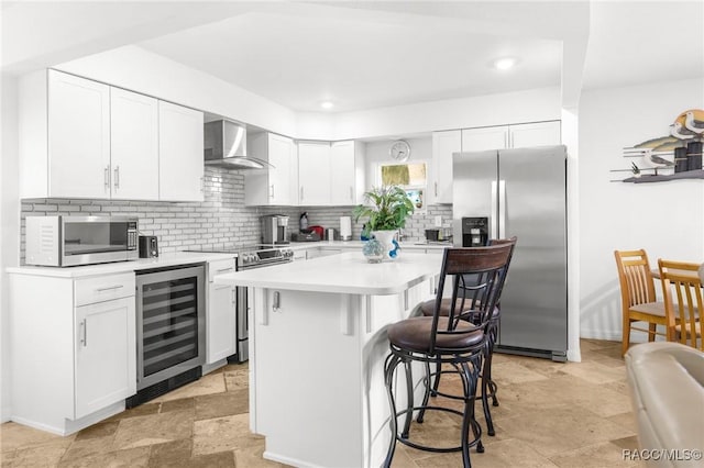 kitchen with a breakfast bar, stainless steel appliances, a center island, wine cooler, and wall chimney exhaust hood