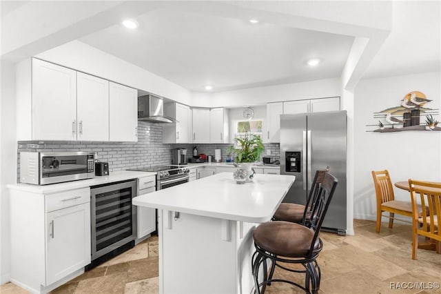 kitchen with wine cooler, wall chimney exhaust hood, white cabinetry, appliances with stainless steel finishes, and a kitchen island