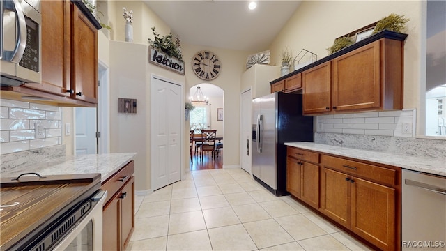 kitchen featuring light stone counters, a notable chandelier, vaulted ceiling, and appliances with stainless steel finishes