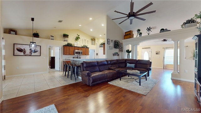 living room featuring light wood-type flooring, decorative columns, high vaulted ceiling, and ceiling fan