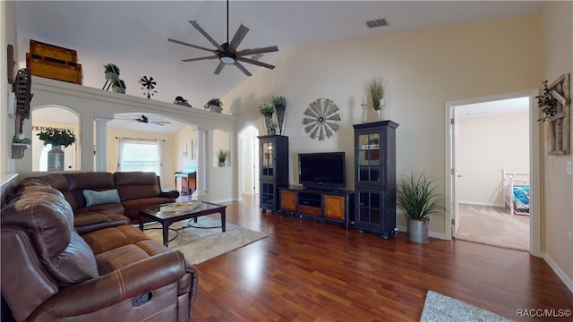 living room with ceiling fan, ornate columns, dark wood-type flooring, and high vaulted ceiling