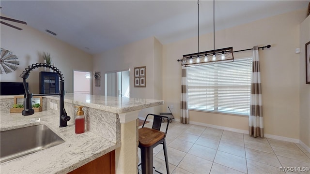 kitchen with sink, hanging light fixtures, vaulted ceiling, light stone counters, and a breakfast bar area